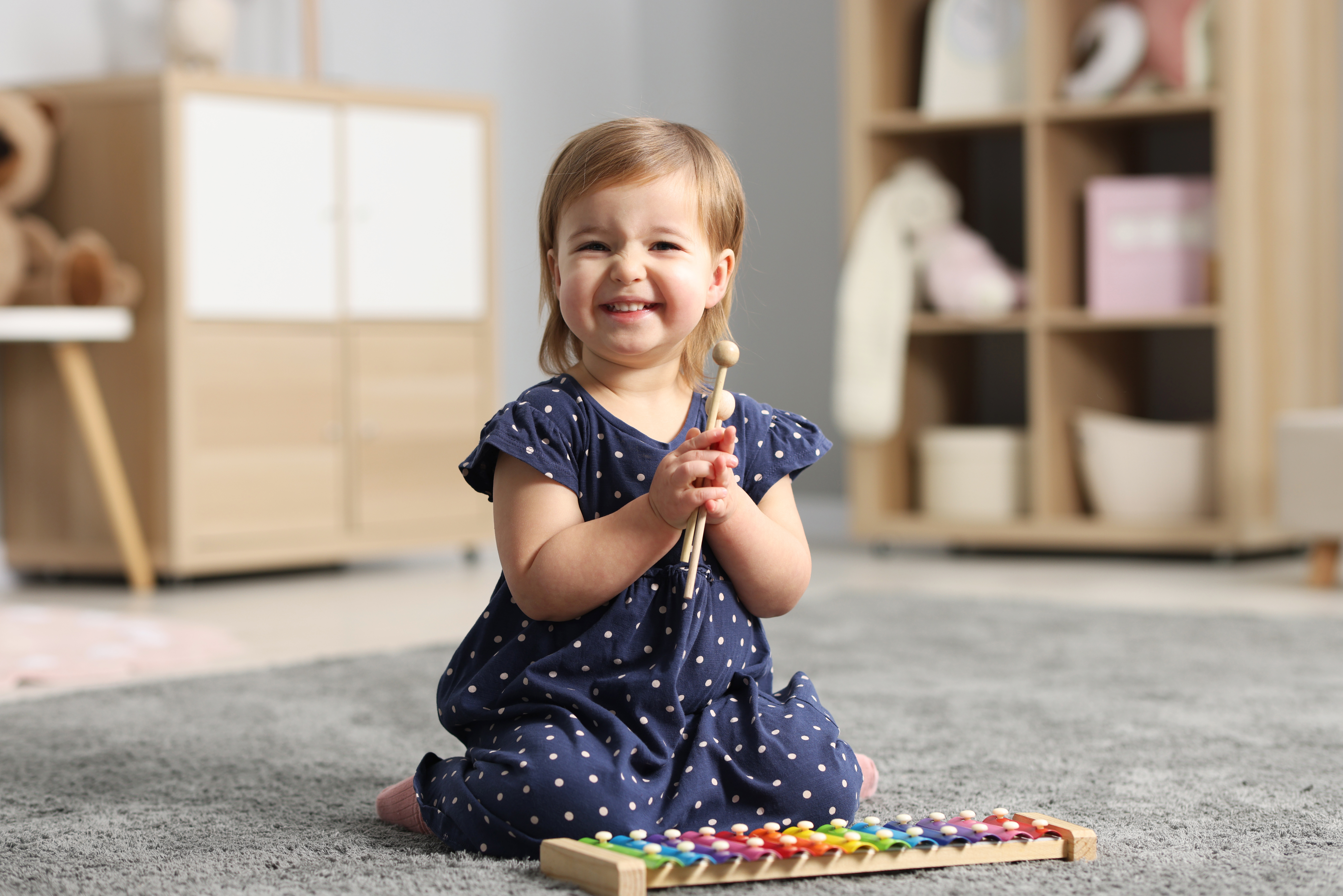 Niña pequeña jugando con un xilófono de colores, disfrutando de una actividad musical en el aula.